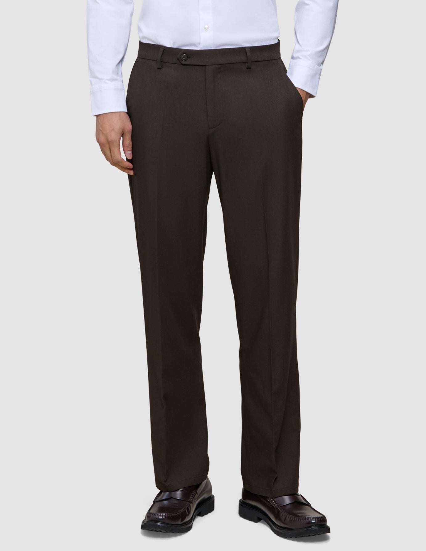 En person iført en hvid skjorte, Motion Suit-bukser i model Relaxed i farven Cognac og loafers.